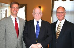 A photo of three men standing shoulder-to-shoulder, wearing dress jackets, white shirts, and ties. The man on the left has a red tie, the man in the middle a blue tie, and the man on the right a striped yellow-and-black tie.