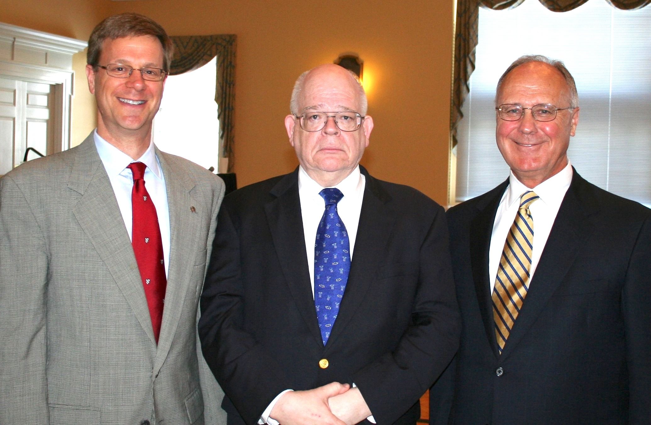 A photo of three men standing shoulder-to-shoulder, wearing dress jackets, white shirts, and ties. The man on the left has a red tie, the man in the middle a blue tie, and the man on the right a striped yellow-and-black tie.