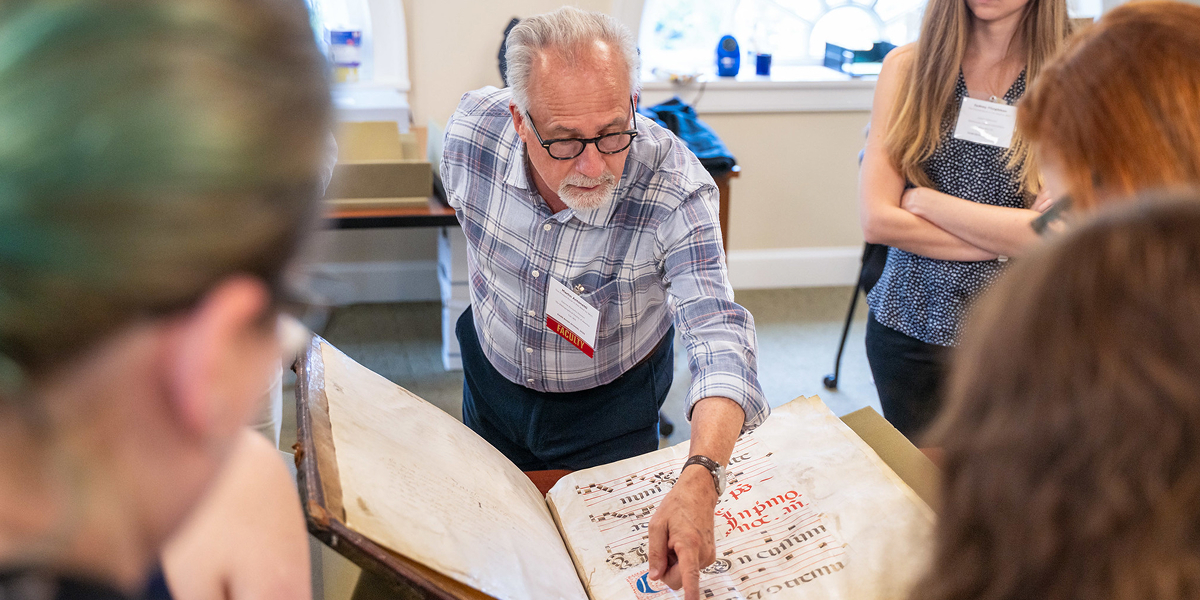 An RBS faculty member points at details of an oversized medieval musical manuscript while students look on