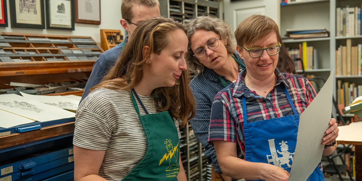 Four people in aprons looking at polymer plate printing.