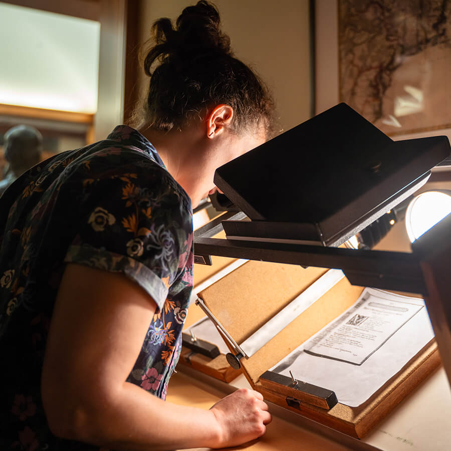 Student examining details of an old print using microscope machine.