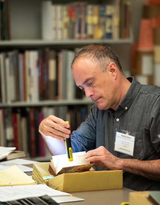 Man at table examining rare book with flashlight
