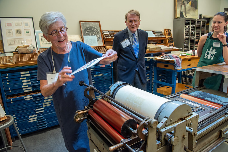 Three people examining a paper around a printing press