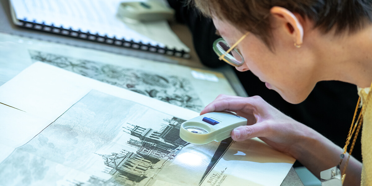 Student at Rare Book School examines a printed illustration with a handheld magnifying loupe to study the fine details of the image and paper texture.