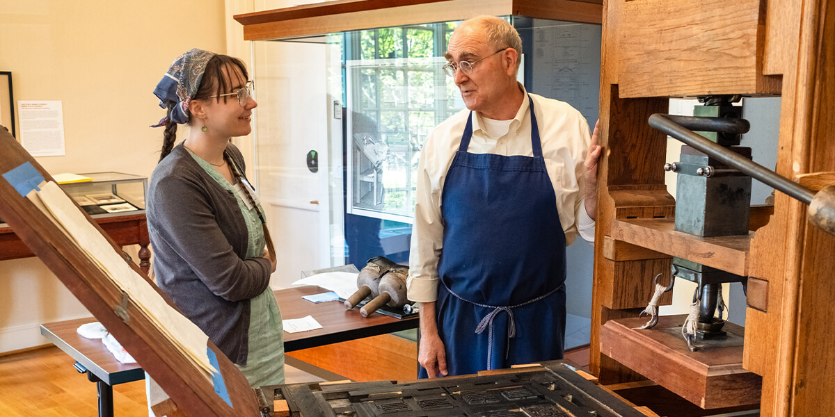 Teacher explaining printing press machine to student.
