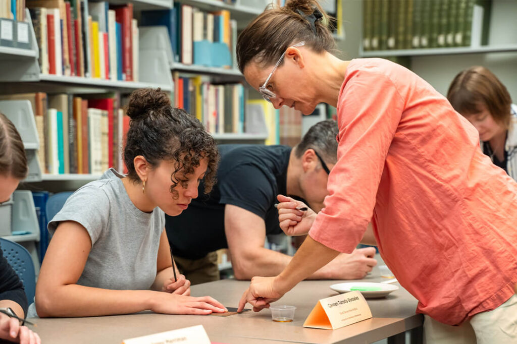 Teacher helping student through process of leather tooling/finishing used in traditional bookbinding