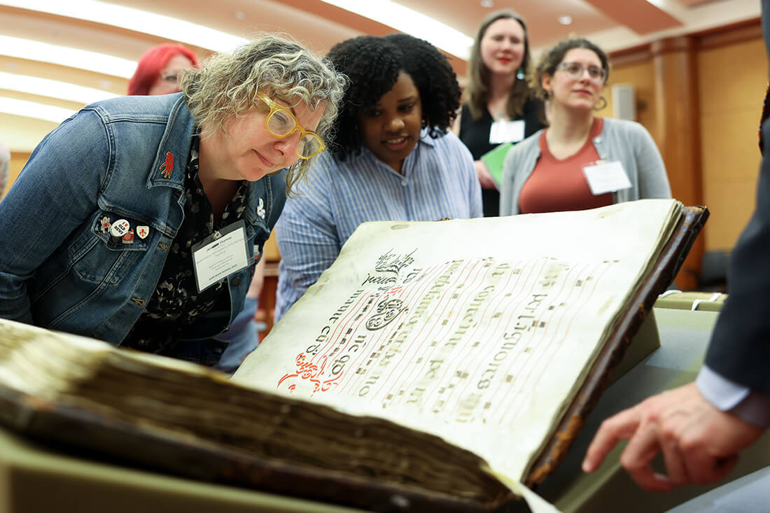 Group of students examining a large, rare book on display.