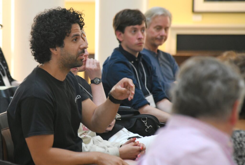 A man gestures as he asks a question while seated in an audience
