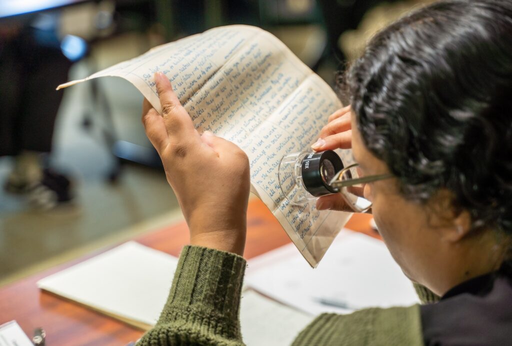 A student examines a hand-written text with a hand-held magnifying glass