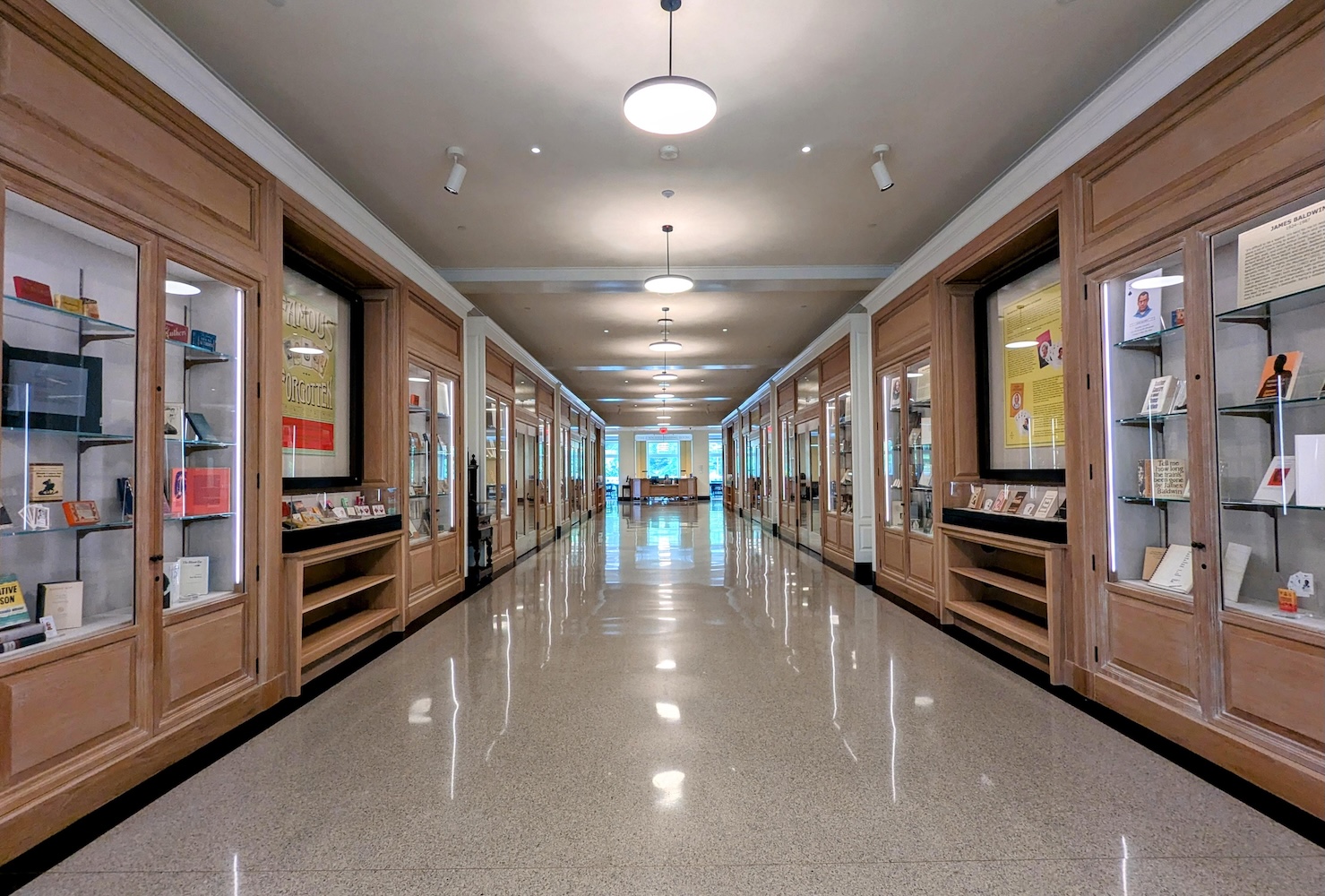 A long hallway with reflective stone tile floors is flanked on both sides by wooden display cases with glass fronts.