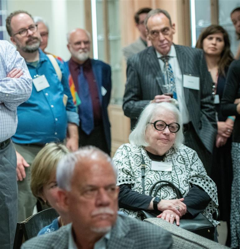 Photo of a group of people standing and sitting as they listen to an off-screen speaker.