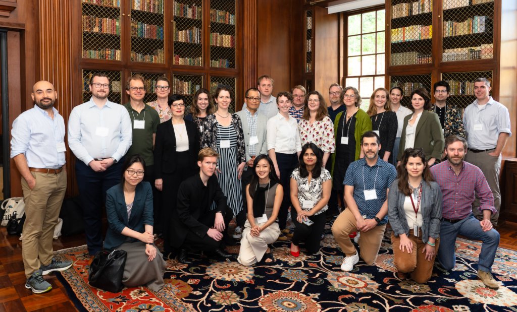 Photo of a group of people posing together in a room lined with wood-paneled bookshelves and with an ornate floral rug.