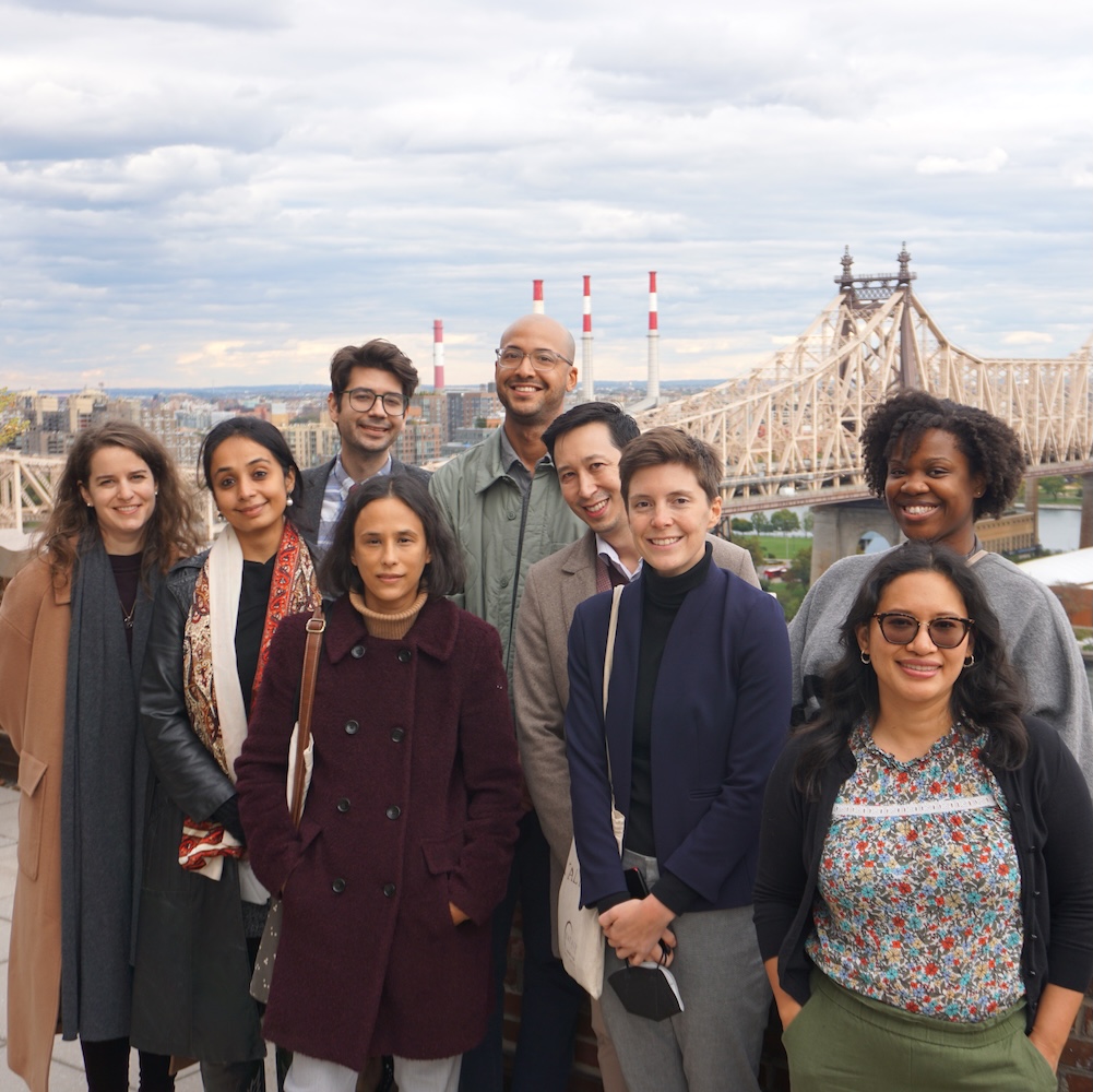 A group of people stand on a rooftop in New York City, with a bridge visible behind them