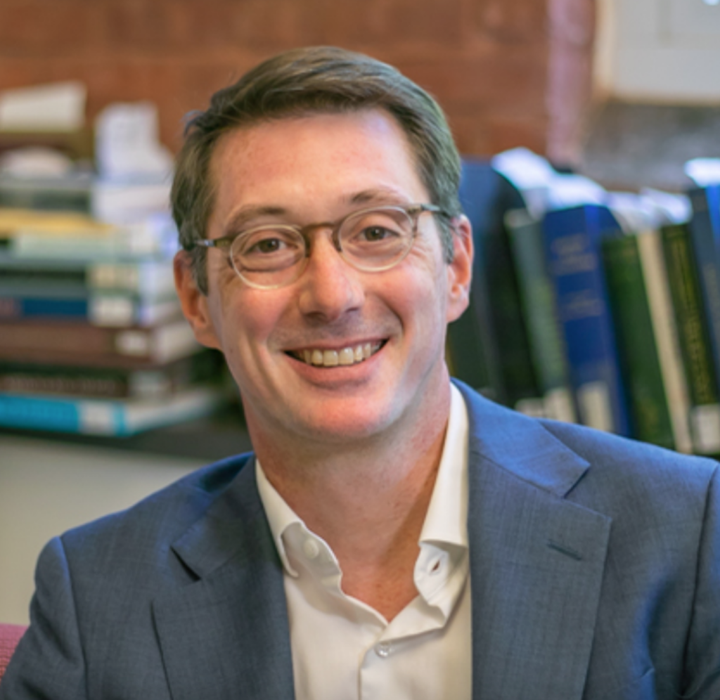 Headshot of a man with glasses in front of a shelf of books
