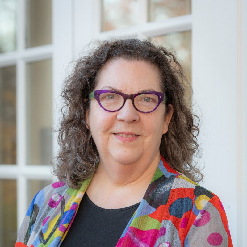 Headshot of a brown-haired woman with a colorful top and green-and-purple-rimmed glasses