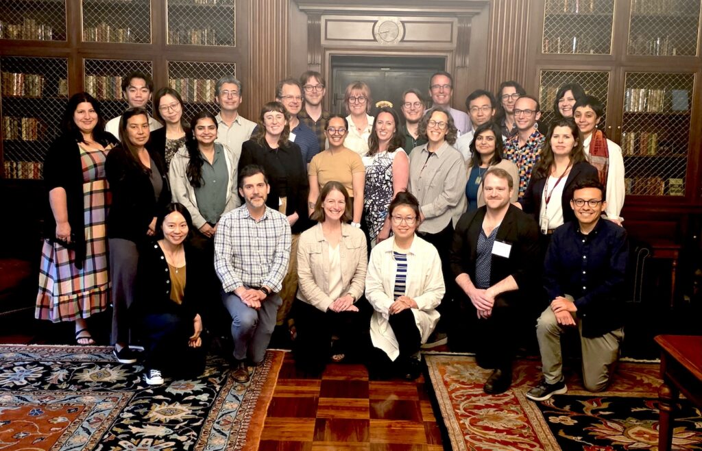 A group of about 25 people pose together in front of dark wood bookshelves.